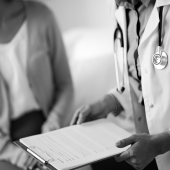 Black and white image of a doctor reading notes to a patient