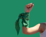 Green background with a person holding their fist up with a green bandana in solidarity.
